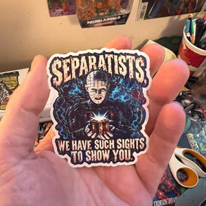 May include: A die-cut sticker featuring a dark, horror-themed illustration of a pale, pin-headed figure holding a glowing puzzle box, surrounded by blue chains. The text SEPARATISTS is at the top, and WE HAVE SUCH SIGHTS TO SHOW YOU is at the bottom.