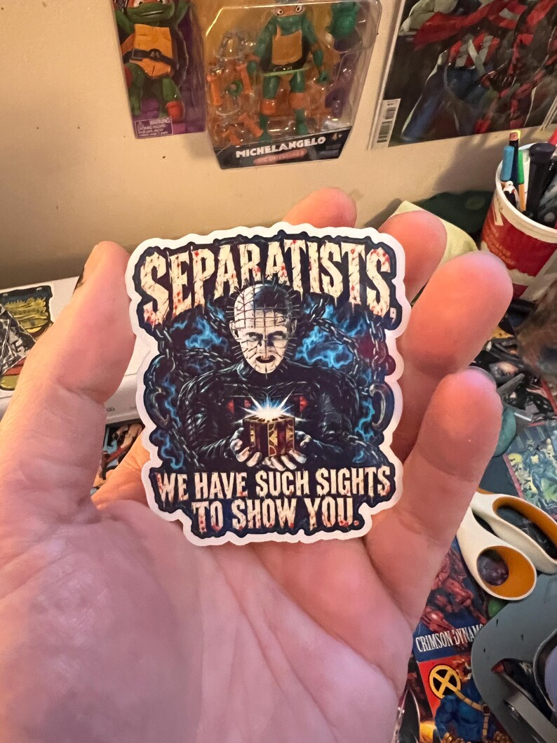 May include: A die-cut sticker featuring a dark, horror-themed illustration of a pale, pin-headed figure holding a glowing puzzle box, surrounded by blue chains. The text SEPARATISTS is at the top, and WE HAVE SUCH SIGHTS TO SHOW YOU is at the bottom.