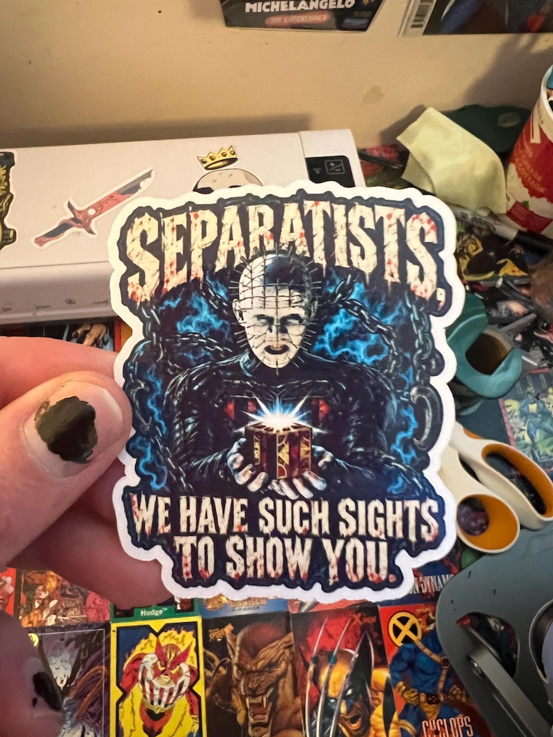 May include: A die-cut sticker featuring a horror character with a pin-covered head, surrounded by blue energy and chains, holding a glowing puzzle box. The text SEPARATISTS is at the top, and WE HAVE SUCH SIGHTS TO SHOW YOU is at the bottom in red.