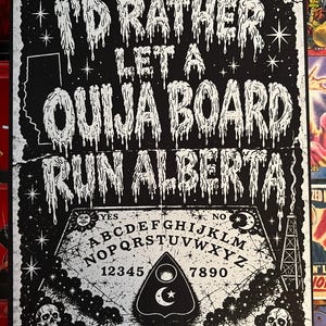 May include: A black and white rectangular poster featuring the text I'D RATHER LET A OUIJA BOARD RUN ALBERTA in a dripping font. The design includes a Ouija board graphic with letters, numbers, a planchette, skulls, stars, and an oil derrick.