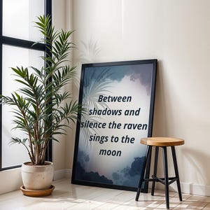 Puede incluir: Una impresión artística enmarcada con el texto "Entre sombras y silencio el cuervo canta a la luna" se apoya contra una pared. Un taburete de madera con patas negras está cerca. Una planta en maceta con hojas verdes está en la esquina.
