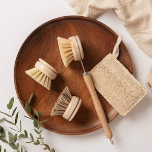 May include: Four wooden dish brushes with natural bristles, a loofah sponge, and a wooden handle with a metal scrubber on a wooden tray.