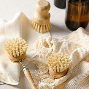 May include: Two natural bristle dish brushes with wooden handles and a white cloth. The brushes are made of natural materials and are designed for cleaning dishes.