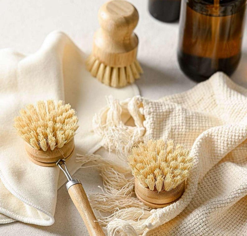 May include: Two natural bristle dish brushes with wooden handles and a white cloth. The brushes are made of natural materials and are designed for cleaning dishes.