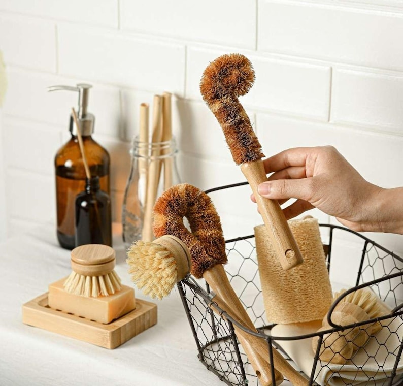 May include: A set of brown and natural colored kitchen cleaning brushes with wooden handles. The brushes are in a wire basket with a natural loofah sponge.