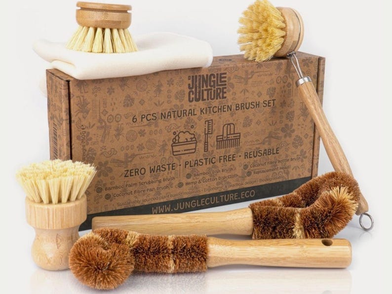 May include: A set of six natural kitchen brushes in a cardboard box. The brushes are made of bamboo, coconut fiber, and hemp. The box has a brown and white design with the text "Jungle Culture" and "6 PCS NATURAL KITCHEN BRUSH SET".