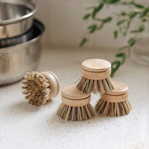 May include: Four natural bristle dish scrubbers with wooden handles. The scrubbers are stacked on top of each other.