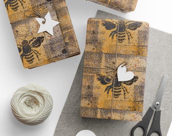 May include: Gift-wrapped packages with a bee design on newsprint-style paper. Each package is tied with twine and adorned with a white star or heart-shaped tag. A spool of twine, scissors, and blank tags are also present.