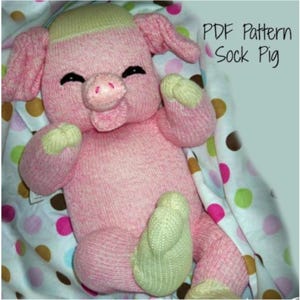 May include: A pink sock pig with a light green nose and light green feet. The pig is lying on a white and brown polka dot blanket. The text "PDF Pattern Sock Pig" is in the upper right corner of the image.