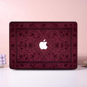 Könnte beinhalten: Burgunderfarbene Laptop-Hülle mit floralem Muster und weißem Apple-Logo. Die Hülle hat eine rechteckige Form mit abgerundeten Ecken und einem dunklen Rand. Das florale Design ist in einem dunkleren Burgunderfarbton gehalten.