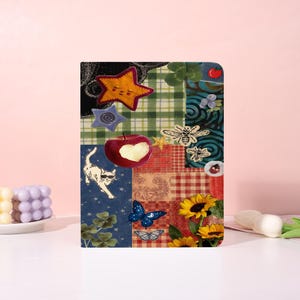 May include: A decorative notebook with a patchwork design featuring a star, apple, cat, butterflies, bees, and sunflowers. The notebook has a variety of patterns and colours, including green plaid, red paisley, and blue floral.