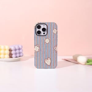 May include: A smartphone case with a blue and red striped design, decorated with heart and diamond-shaped patches. The patches feature text and floral motifs. The case is designed to fit a mobile phone.