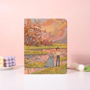 Könnte beinhalten: Ein rechteckiges Notizbuch mit einer farbenfrohen Illustration einer großen mechanischen Burg, einer Berglandschaft und zwei Figuren, die zusammen auf einem Feld stehen. Das Bild zeigt zudem eine kleine orangefarbene Flamme und eine Spiegelung im Wasser.