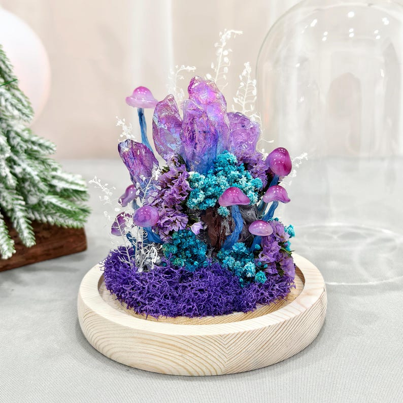 May include: A decorative terrarium featuring a cluster of purple crystals, miniature mushrooms, and blue and purple flowers. The arrangement sits on a bed of purple moss within a wooden base, covered by a glass dome.