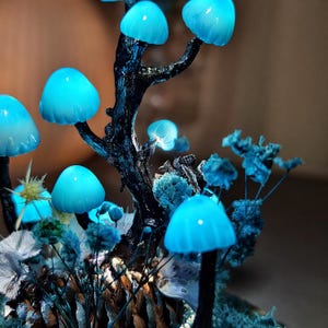 May include: A blue glowing mushroom lamp with a tree trunk base and dried flowers. The mushrooms are made of glass and have a frosted finish.