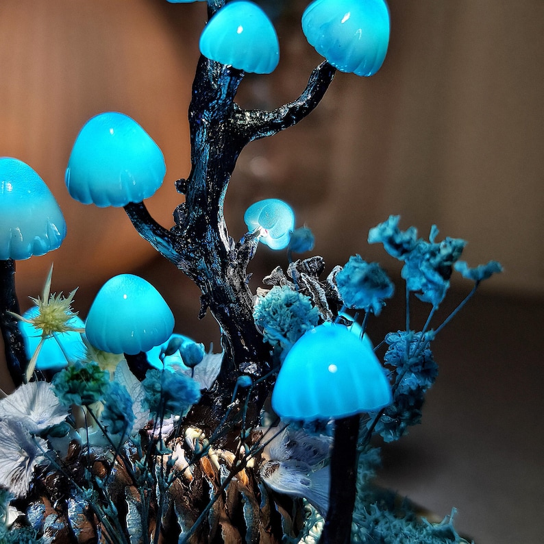 May include: A blue glowing mushroom lamp with a tree trunk base and dried flowers. The mushrooms are made of glass and have a frosted finish.