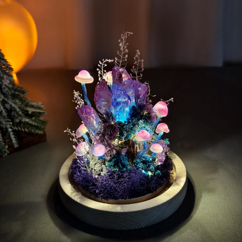 May include: A decorative illuminated mushroom and crystal sculpture. The sculpture features glowing pink mushrooms, purple crystals, and blue and purple moss, all set in a wooden base. The crystals emit a blue light, creating a magical ambiance.