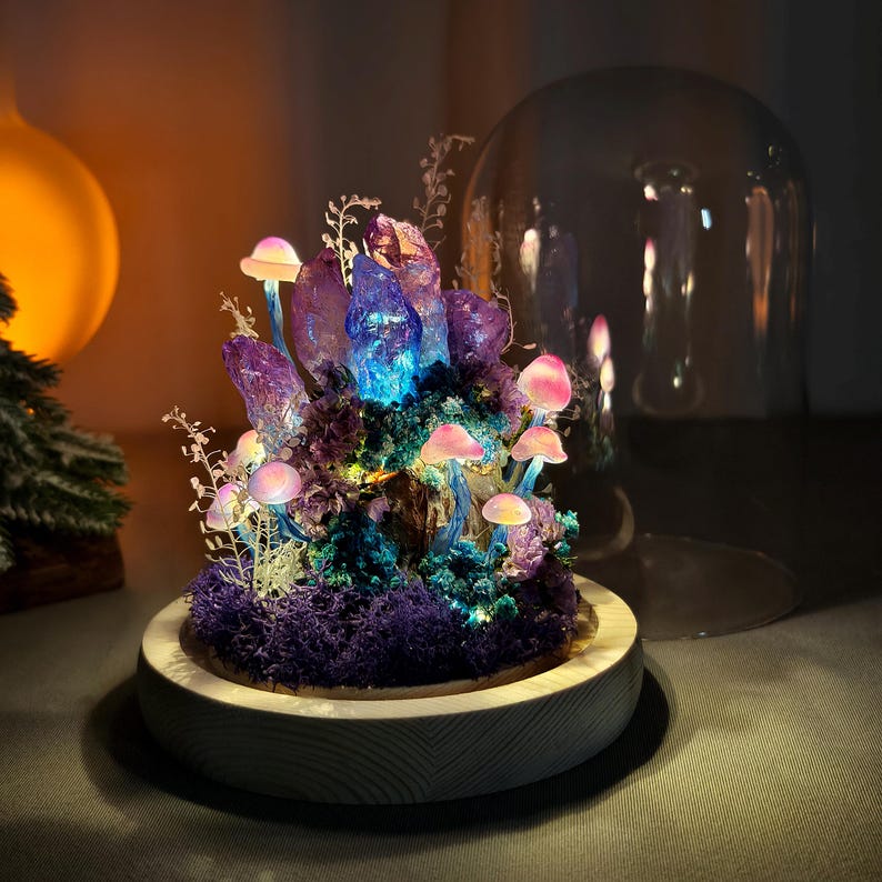 May include: A fantasy-themed terrarium with glowing mushrooms, purple crystals, and moss. The miniature scene is set in a wooden base and covered by a glass dome. The mushrooms have pink caps and blue stems.