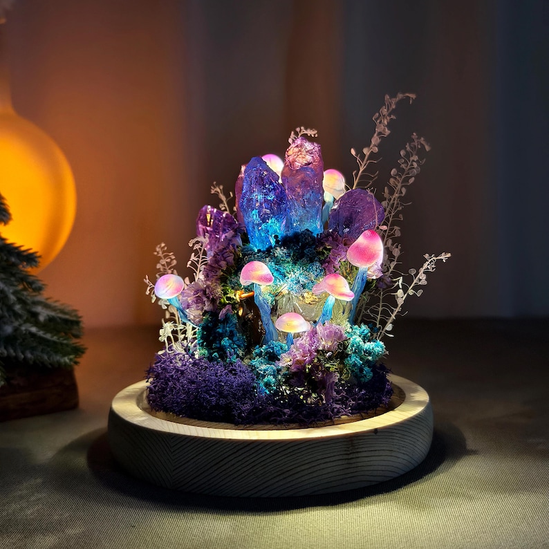 May include: A decorative illuminated mushroom and crystal sculpture. The sculpture features glowing pink and white mushrooms, purple crystals, and blue and purple moss, all set within a wooden base. The lighting creates a magical, fantasy-like atmosphere.