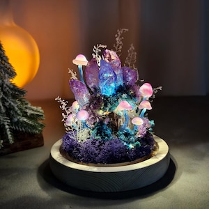 May include: A decorative illuminated mushroom and crystal sculpture. The sculpture features a cluster of purple crystals with blue and purple lighting, surrounded by pink mushrooms and purple moss, set on a wooden base.
