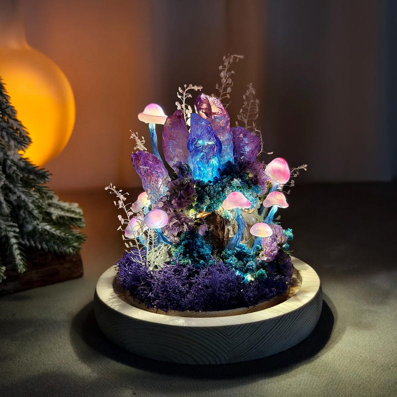 May include: A decorative illuminated mushroom and crystal sculpture. The sculpture features a cluster of purple crystals with blue and purple lighting, surrounded by pink mushrooms and purple moss, set on a wooden base.