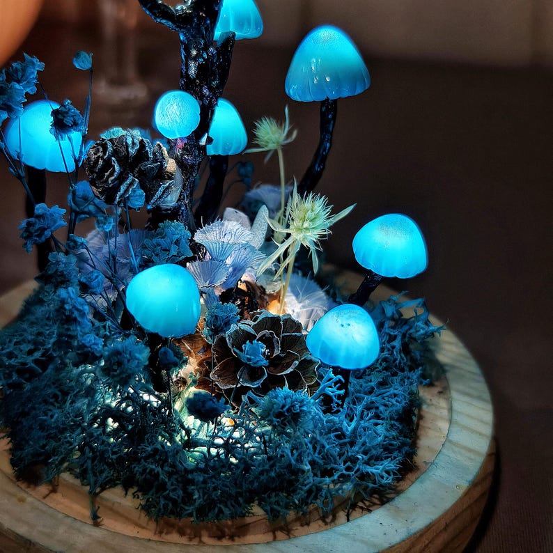 May include: A glowing blue mushroom forest scene in a wooden planter. The mushrooms are made of resin and have a realistic appearance. The planter is filled with moss and other greenery.