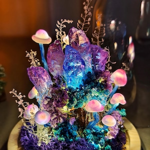 May include: A decorative terrarium featuring a cluster of purple and blue crystals, surrounded by pink mushrooms and dried flowers. The base is a wooden circle, and the overall effect is whimsical and enchanting.