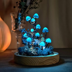 May include: A glowing blue mushroom forest scene in a wooden planter. The mushrooms are made of glass and are lit from within, creating a magical effect.