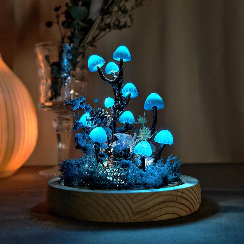 May include: A glowing blue mushroom forest scene in a wooden planter. The mushrooms are made of glass and are lit from within, creating a magical effect.