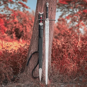May include: A longsword with a double-edged steel blade, a silver crossguard, and a black grip with a silver pommel. Beside the sword stands a black leather scabbard featuring silver metal fittings at the throat and a pointed silver chape.