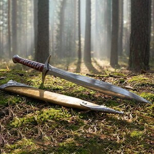 Pu&ograve; includere: Un pugnale argentato e marrone con un'impugnatura rivestita in pelle e un fodero decorativo &egrave; appoggiato su un letto di muschio. La lama presenta un motivo dettagliato. Il fodero &egrave; beige con dettagli argentati. La scena &egrave; ambientata in una foresta.