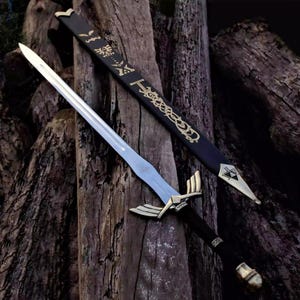 Pu&ograve; includere: Una spada con lama argentata, elsa dorata e manico nero &egrave; appoggiata su una superficie di legno. Un fodero nero con motivi decorativi dorati &egrave; dietro la spada. La spada ha un design dettagliato.