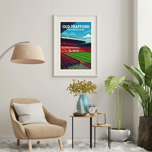 K&ouml;nnte beinhalten: Ein gerahmter Kunstdruck des Old Trafford-Stadions, der Heimat von Manchester United, mit blauem Himmel im Hintergrund. Der Druck zeigt die roten Sitze und den gr&uuml;nen Rasen des Stadions. Der Text "OLD TRAFFORD" und "MANCHESTER UNITED" sind oben zu sehen.