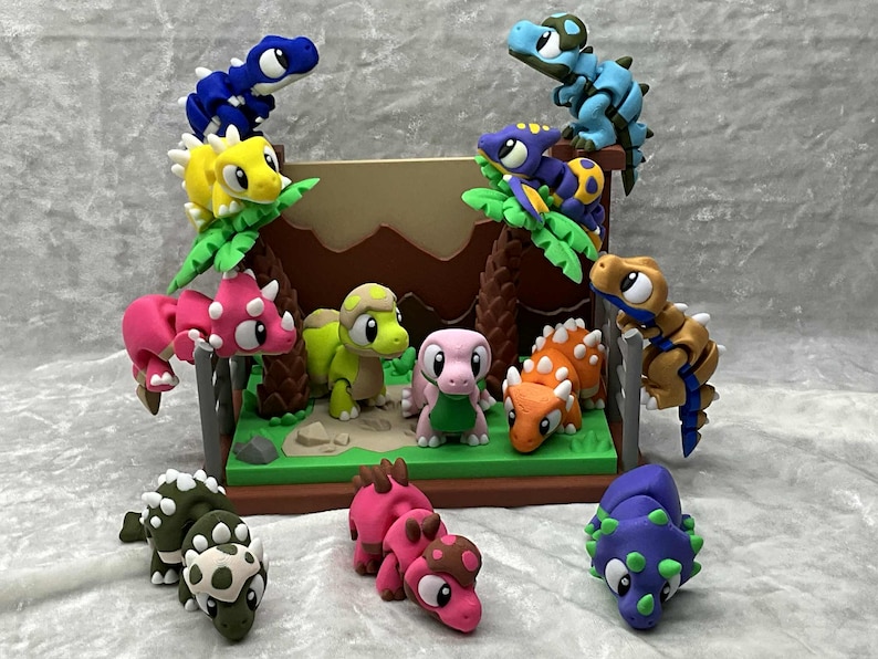May include: A colorful diorama featuring various dinosaur figurines. The dinosaurs are in shades of blue, yellow, pink, orange, green, and purple. Some are perched on faux trees, while others stand on a green base with a brown backdrop.
