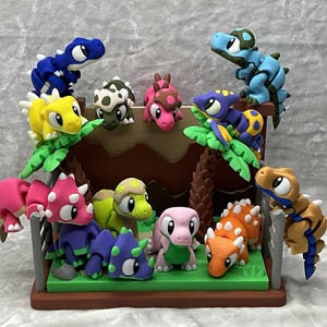 May include: A collection of colorful dinosaur figurines, including blue, yellow, pink, and orange, arranged on a miniature diorama. The scene features a brown structure with green foliage, creating a playful prehistoric theme.