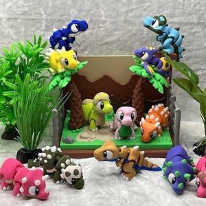 May include: A collection of colorful, handcrafted dinosaur figurines. The scene includes various species in shades of pink, green, blue, yellow, and orange, set against a backdrop of a miniature landscape with trees and foliage. These figurines are likely made of clay.