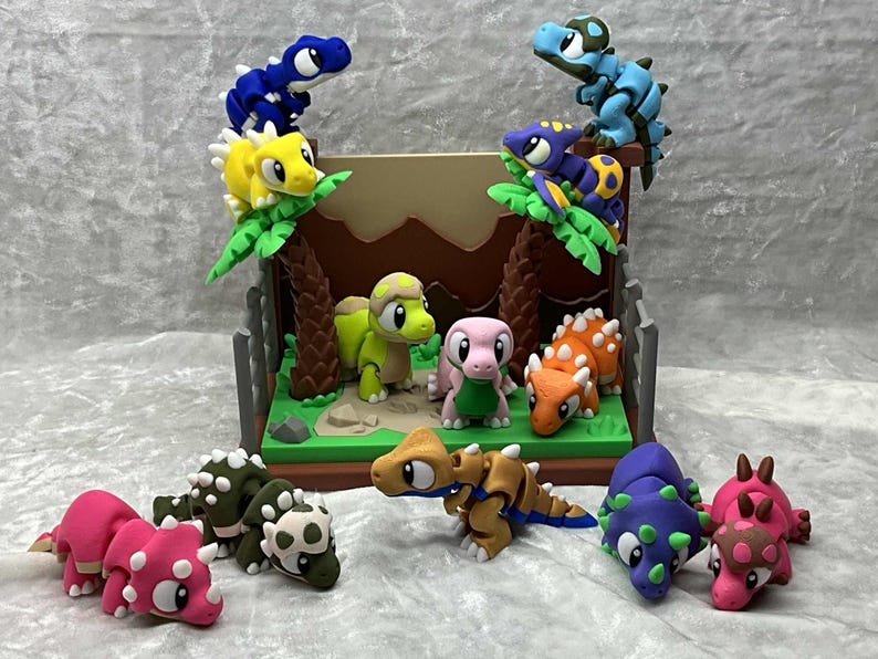 May include: A collection of colorful, handcrafted dinosaur figurines. The scene includes various dinosaurs in shades of blue, yellow, green, pink, and orange, some perched on miniature palm trees. The dinosaurs are arranged in a diorama setting with a brown backdrop.