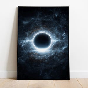 May include: A framed art print showing a black hole in space. The image features a dark, circular void surrounded by swirling blue and white nebulas and bright light. The print is displayed on a white wall above a wooden floor.