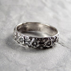 May include: A silver band ring with a floral design. The ring is made of sterling silver and features a delicate floral pattern.