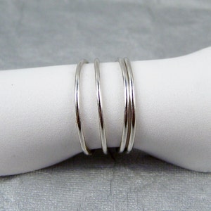 May include: Four silver rings stacked on top of each other. The rings are thin and have a smooth, polished finish.