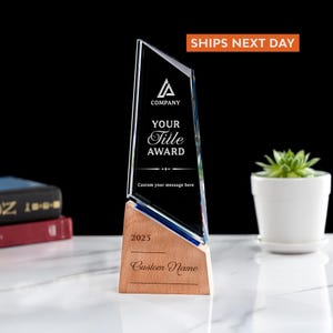 May include: A clear glass award with a wooden base. The award has the text "COMPANY", "YOUR Title AWARD", and "Custom your message here". The base has the text "2025" and "Custom Name". The award is on a white surface.