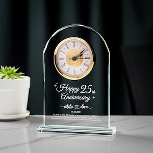 May include: A clear glass anniversary clock with a gold-colored clock face and Roman numerals. The clock is engraved with "Happy 25th Anniversary" and a personalized message. The clock is approximately 6 inches tall.