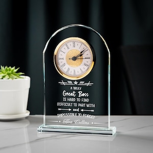 May include: A clear glass desk clock with a gold-tone clock face and Roman numerals. The clock has the text "A Truly Great Boss is hard to find, difficult to part with and impossible to forget" and the name "Ava Collins".