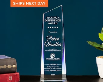 May include: A clear, wedge-shaped glass award featuring an angled top. The front is engraved with the text Making a Difference Award, five stars, Peter Smiths, Code Technology Innovator in Electronics, and the year 2026 in white lettering.