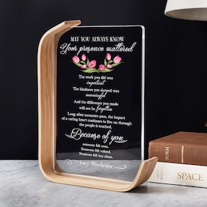 May include: A clear acrylic plaque held in a curved light wood stand. The plaque features pink tulip illustrations and white text that reads: MAY YOU ALWAYS KNOW Your presence mattered. The work you did was important. The kindness you showed was meaningful. And the difference you made will not be forgotten. Long after moments pass, the impact of a caring heart continues to live on through the people it touched. Because of you someone felt seen. Someone felt valued. Someone felt less alone. Lucy Winchester.