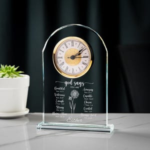 May include: A clear glass clock with a gold-colored clock face and Roman numerals. The clock has the words "god says you are" and inspirational words and Bible verses. The name "Esther" is at the bottom.