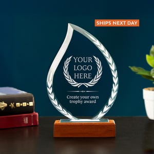 May include: Clear crystal trophy in a teardrop shape with a wooden base. The trophy has a laurel wreath design and the text "YOUR LOGO HERE" and "Create your own trophy award".