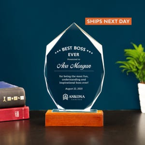 May include: A clear crystal award with the text "BEST BOSS EVER" and the name "Ava Morgan" on a wooden base. The award is a geometric shape with a beveled edge. The text "SHIPS NEXT DAY" is in the top right corner.