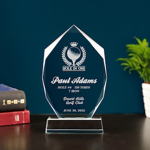 May include: A clear, faceted golf trophy with the words "HOLE IN ONE" and personalized text. The trophy includes the name "Paul Adams", golf details, and the date June 30, 2025. The trophy is on a clear base.