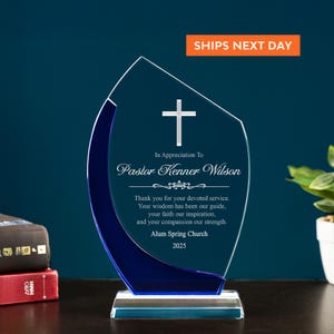 May include: A clear acrylic award with a blue accent and a cross. The text reads "In Appreciation To Pastor Kenner Wilson" and includes a thank you message. The base is rectangular and clear. The award is for Alum Spring Church, 2025.